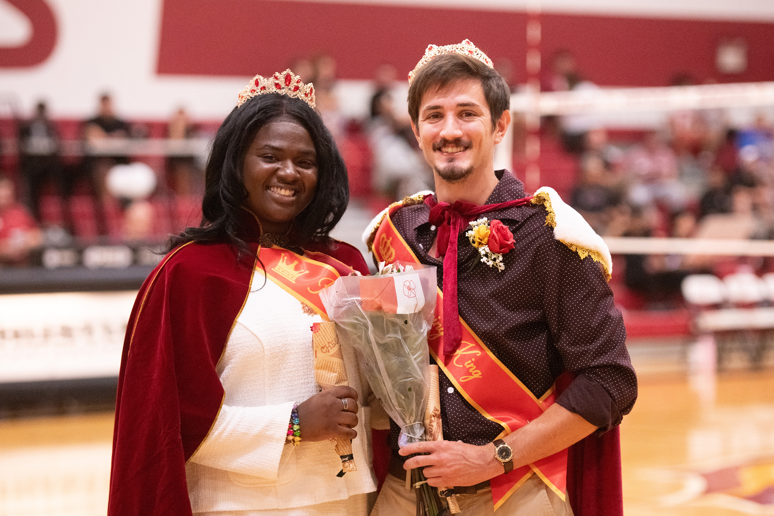 King and queen of homecoming pose for photo wearing crowns and holding flowers.