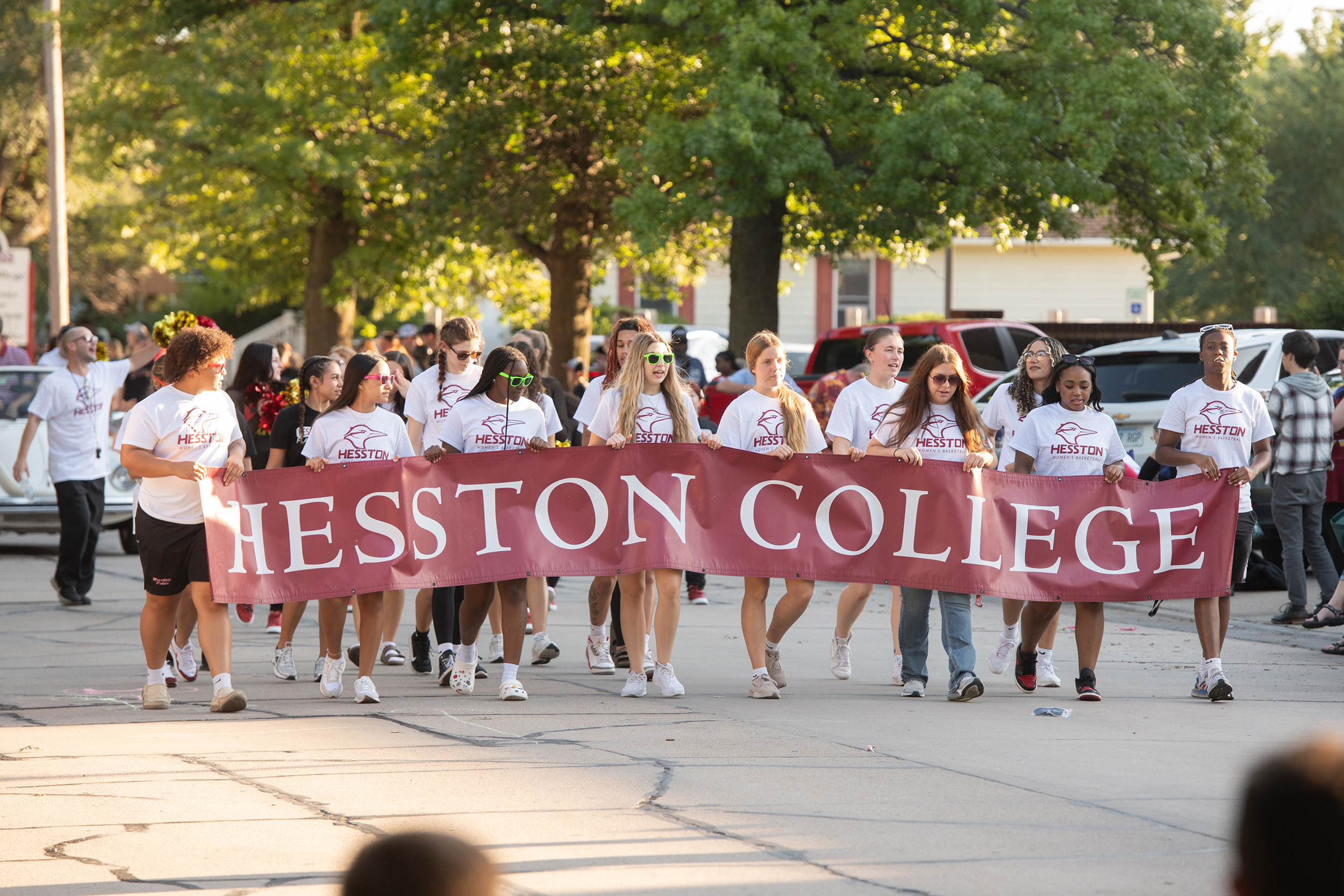 Group of students walking in homecoming parade holding Hesston College banner.