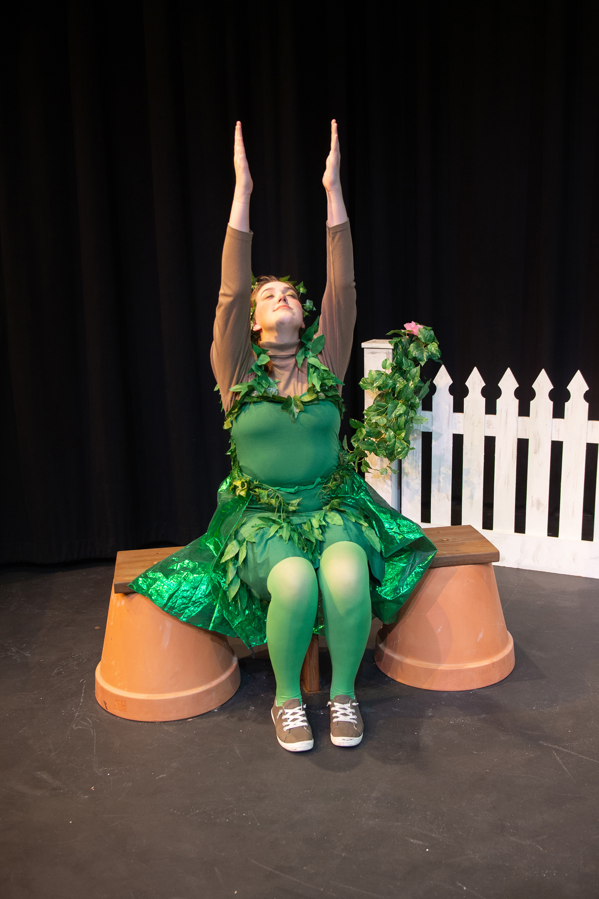 Female student dressed like a plant sits on stage.