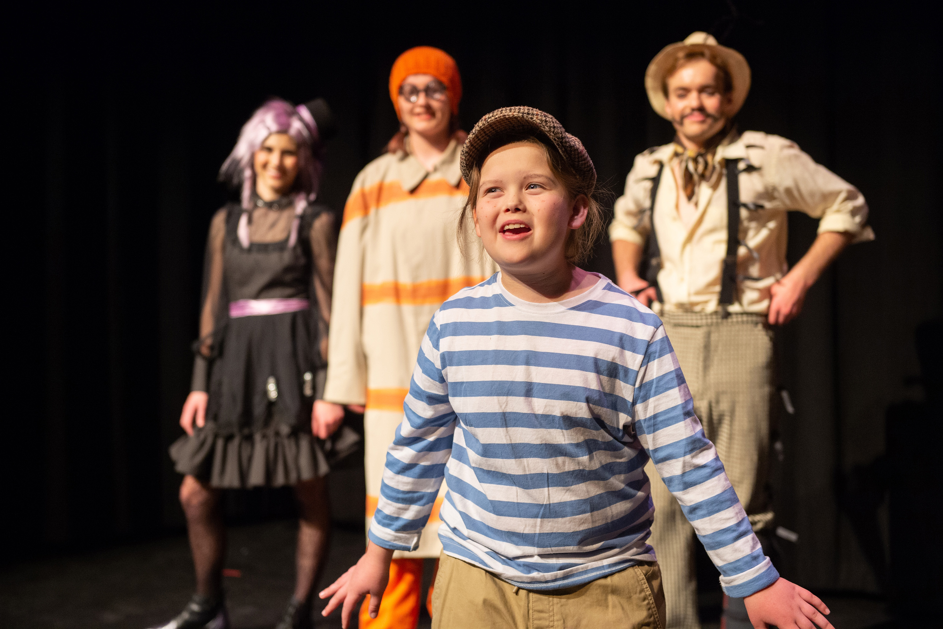 Young boy performs on stage with 3 students standing behind him.