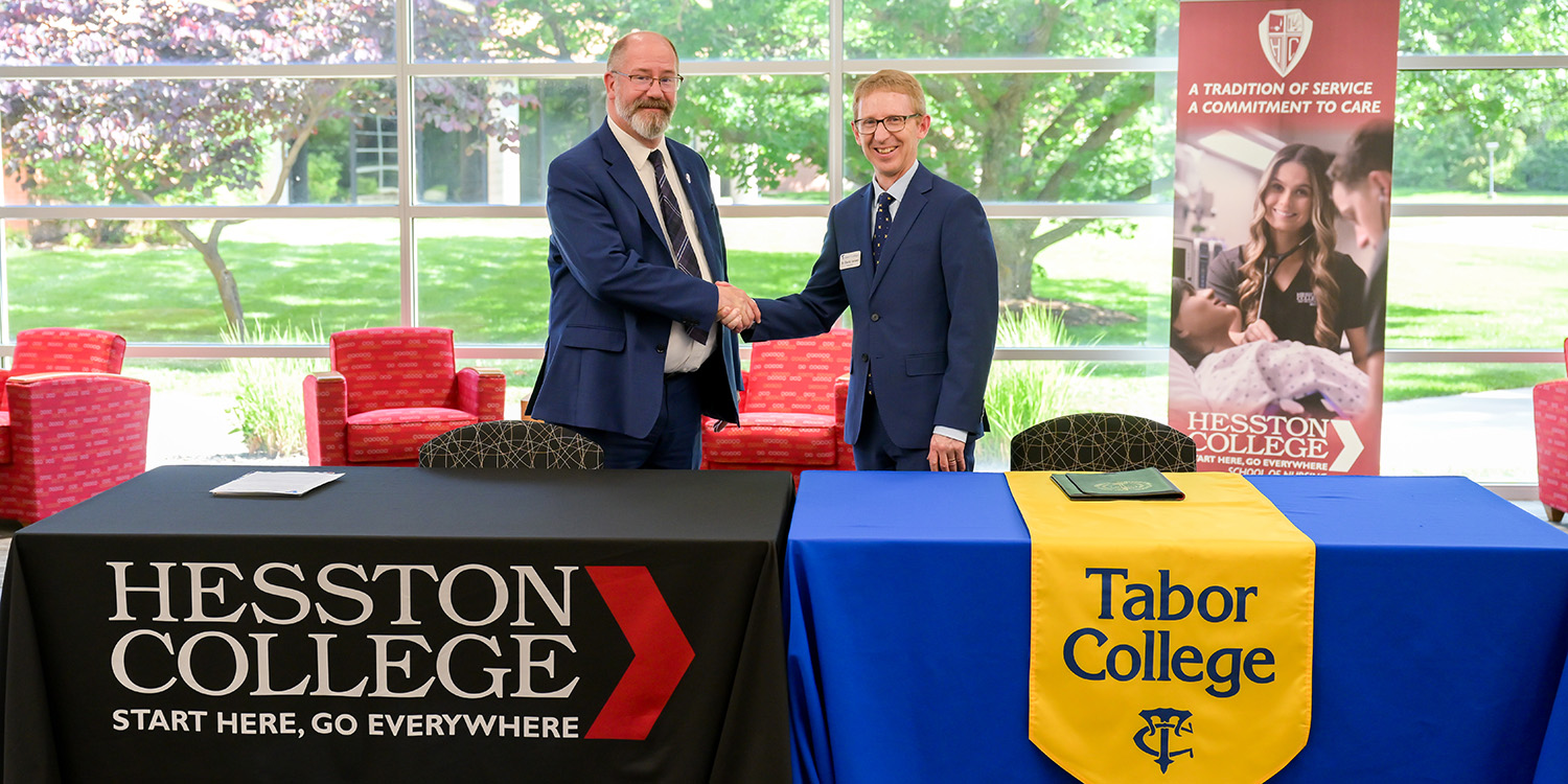 Representatives from Hesston College and Tabor College shake hands.